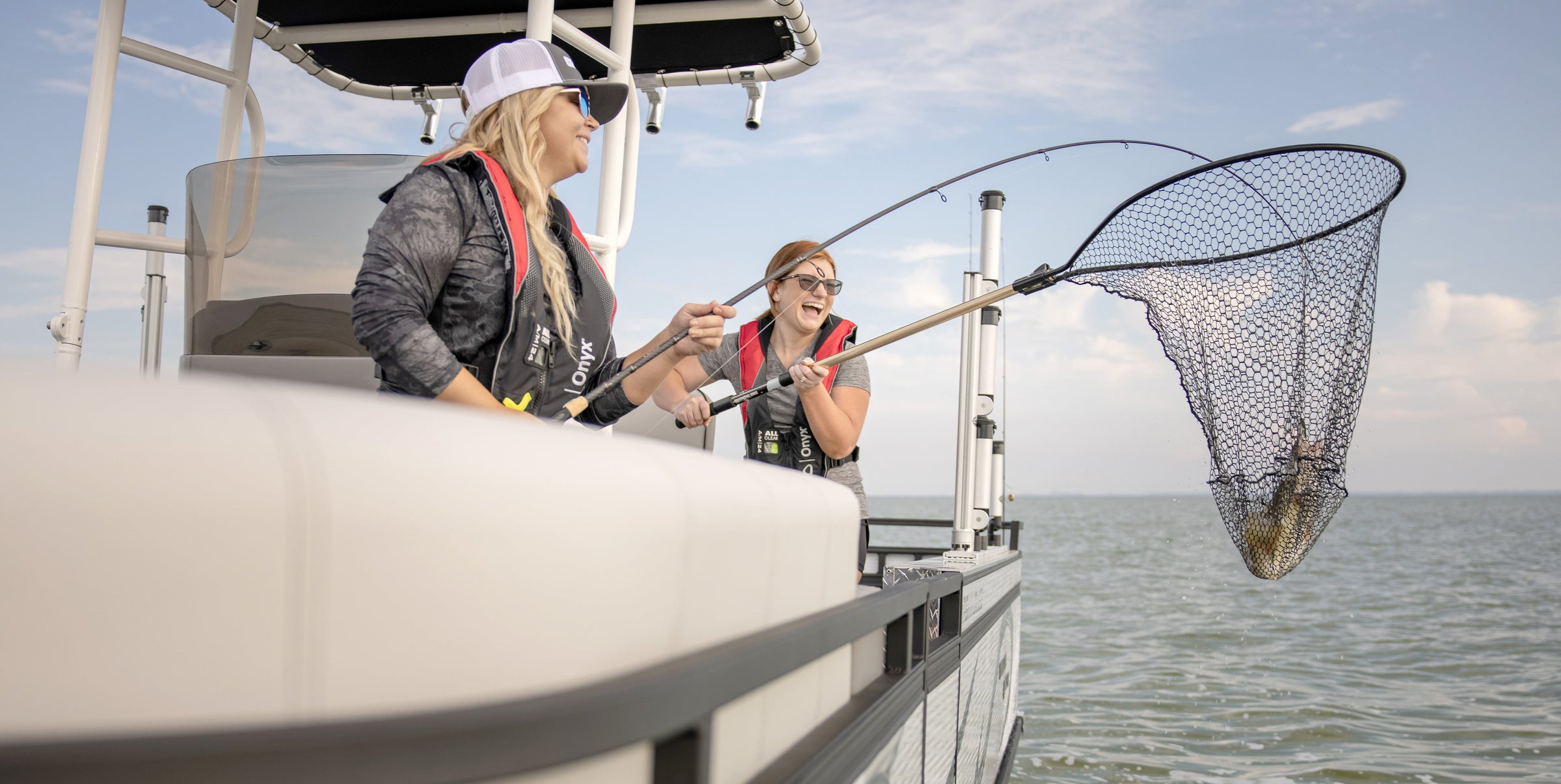 Two fishermen wearing Onyx Inflatable Life Vests pulling in a great catch in their net on the side of their boat.
