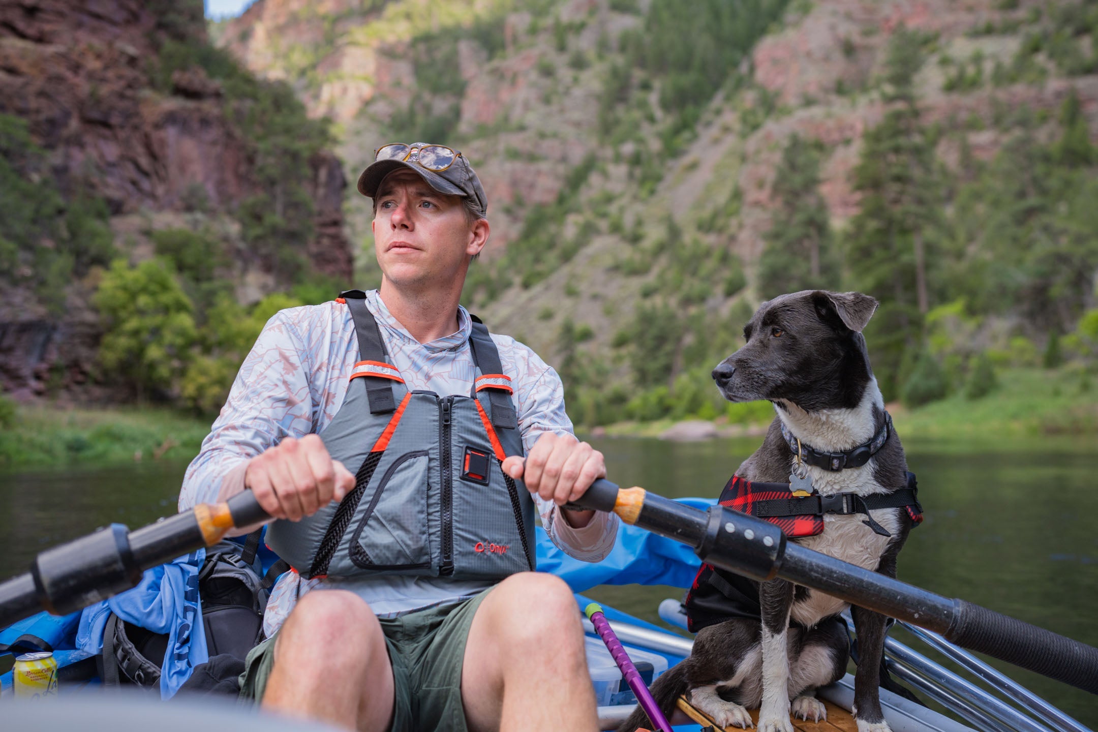 Man wearing an Onyx life jacket while rafting through a red rock canyon. A dog is with him wearing a pet flotation device from Onyx.