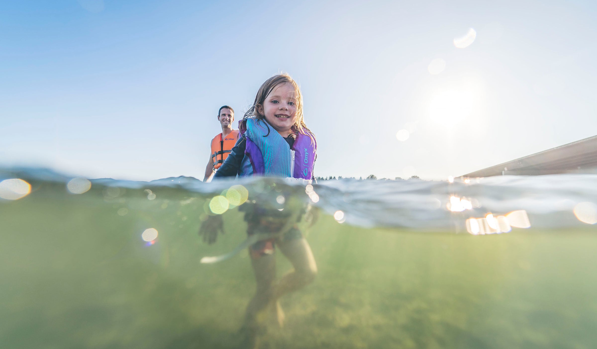Photo of a young girl wearing a Child Life Vest from Onyx. The photo is half above water, half below.