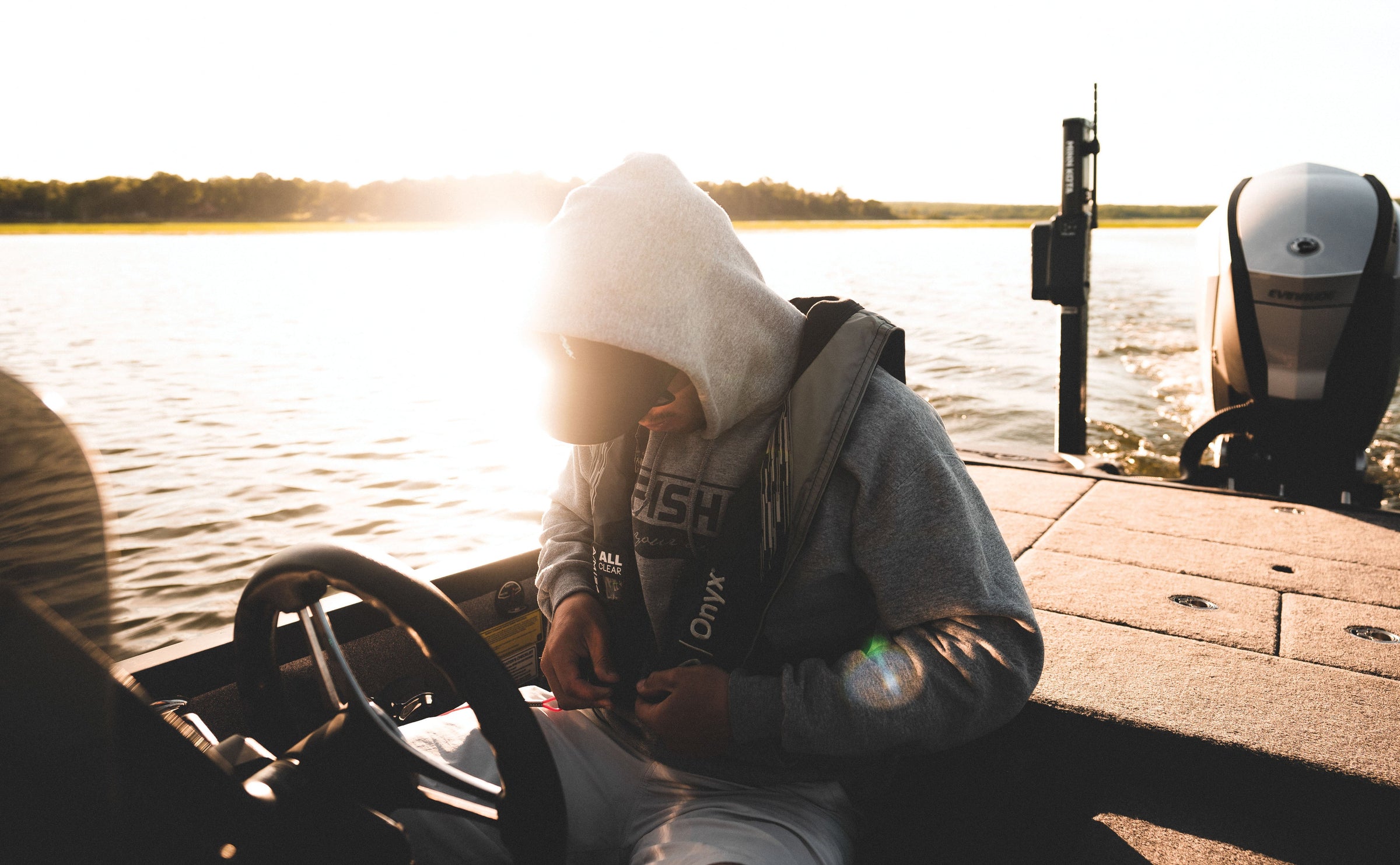 Man sitting his fishing boat tying lures while wearing an inflatable Onyx Life Jacket.