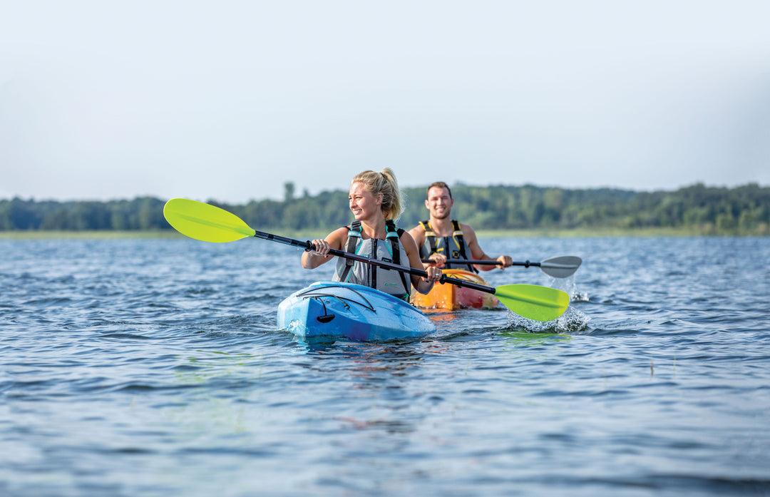 Two Women Kayaking wearing Onyx Personal Flotation Devices on a calm sunny day.