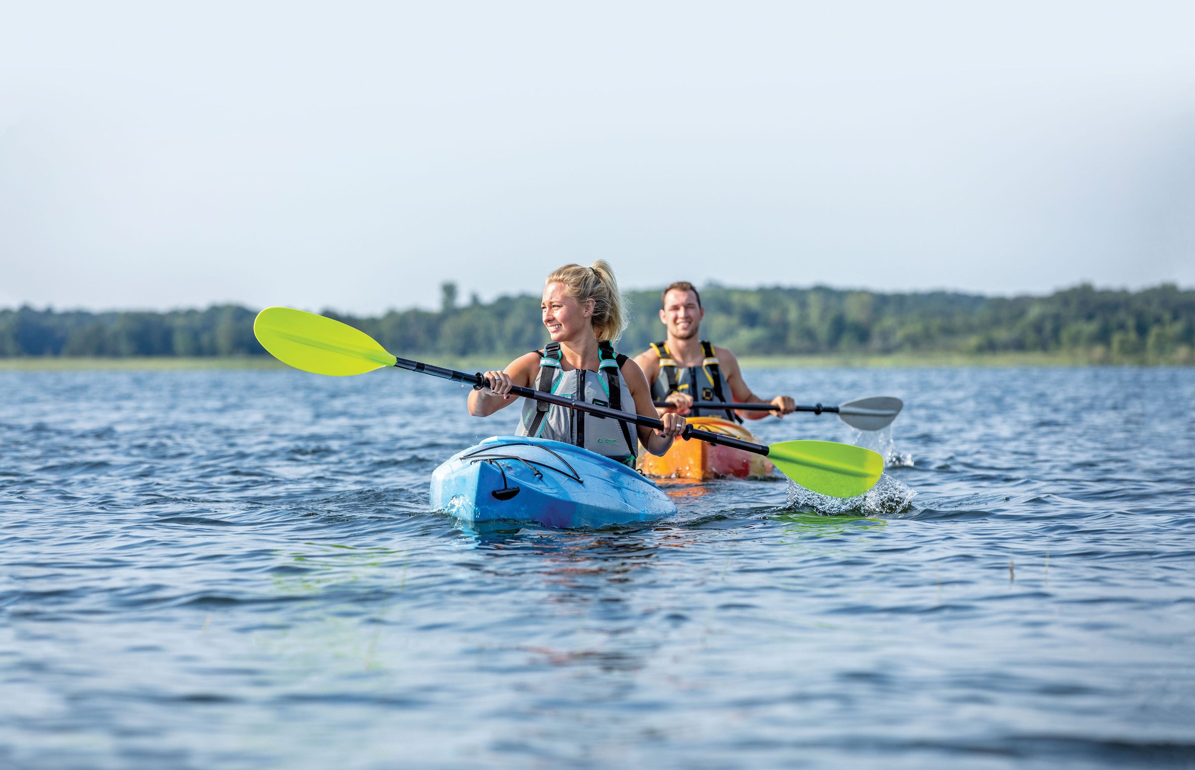 Two Women Kayaking wearing Onyx Personal Flotation Devices on a calm sunny day.