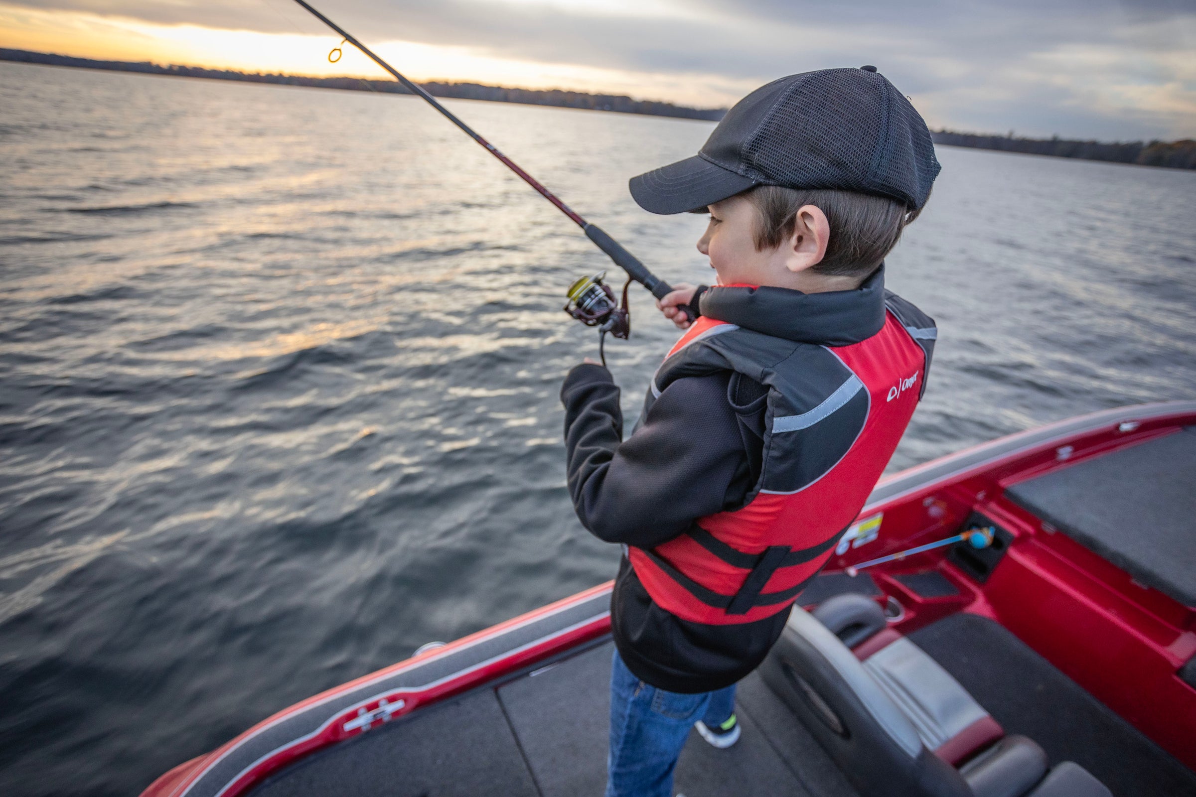 A young child fishing off the side of a fishing boat while wearing a Youth Life Vest from Onyx.