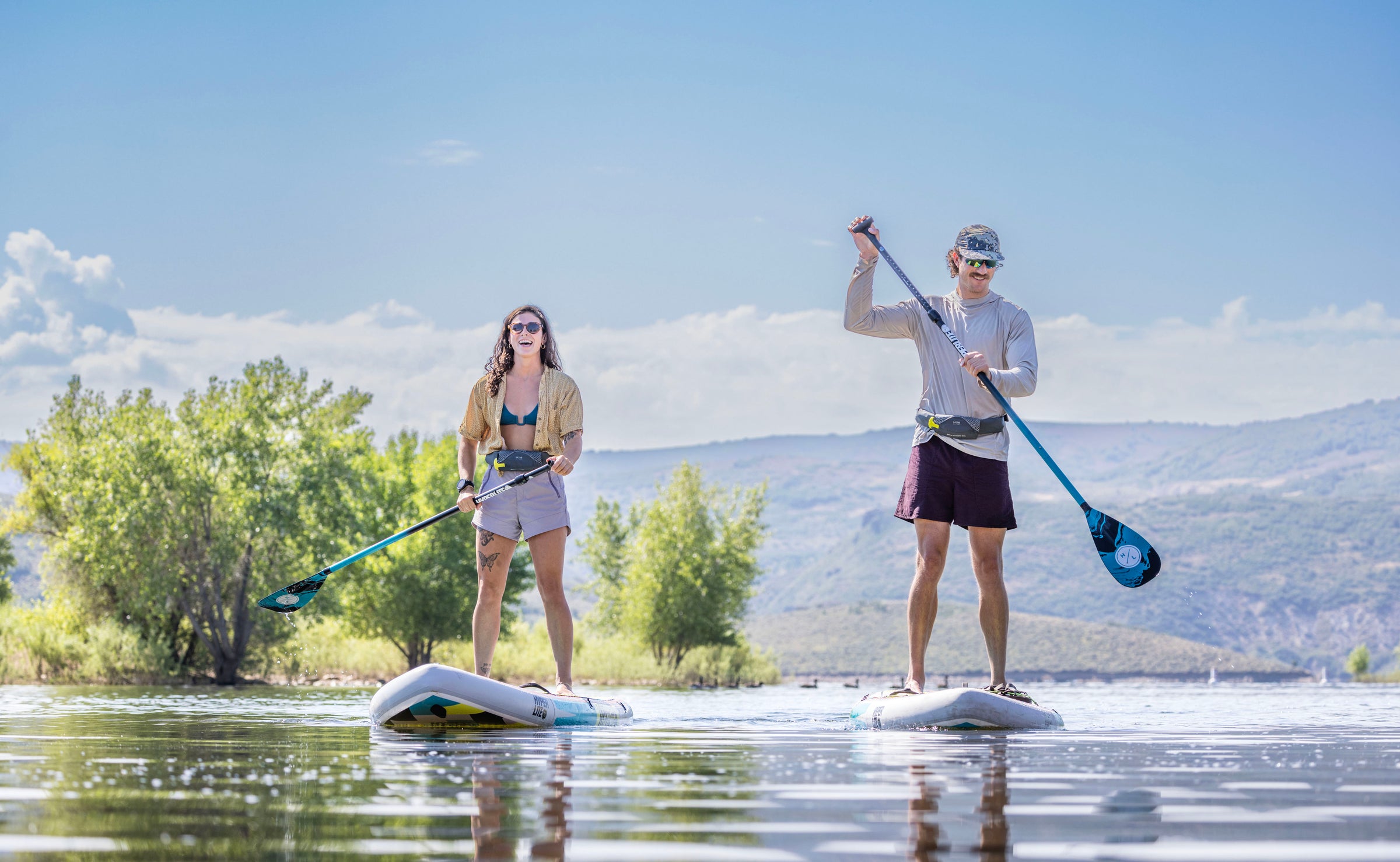Man and woman paddle boarding on a lake wearing Onyx belt pack life jackets.