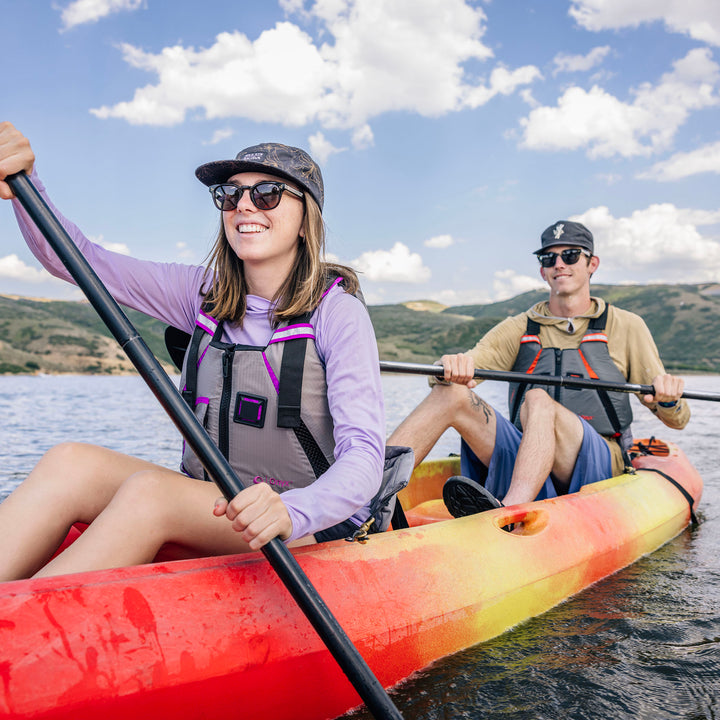 Two kayakers on a lake wearing MoveVent Dynamic Life Jackets under a blue sky.