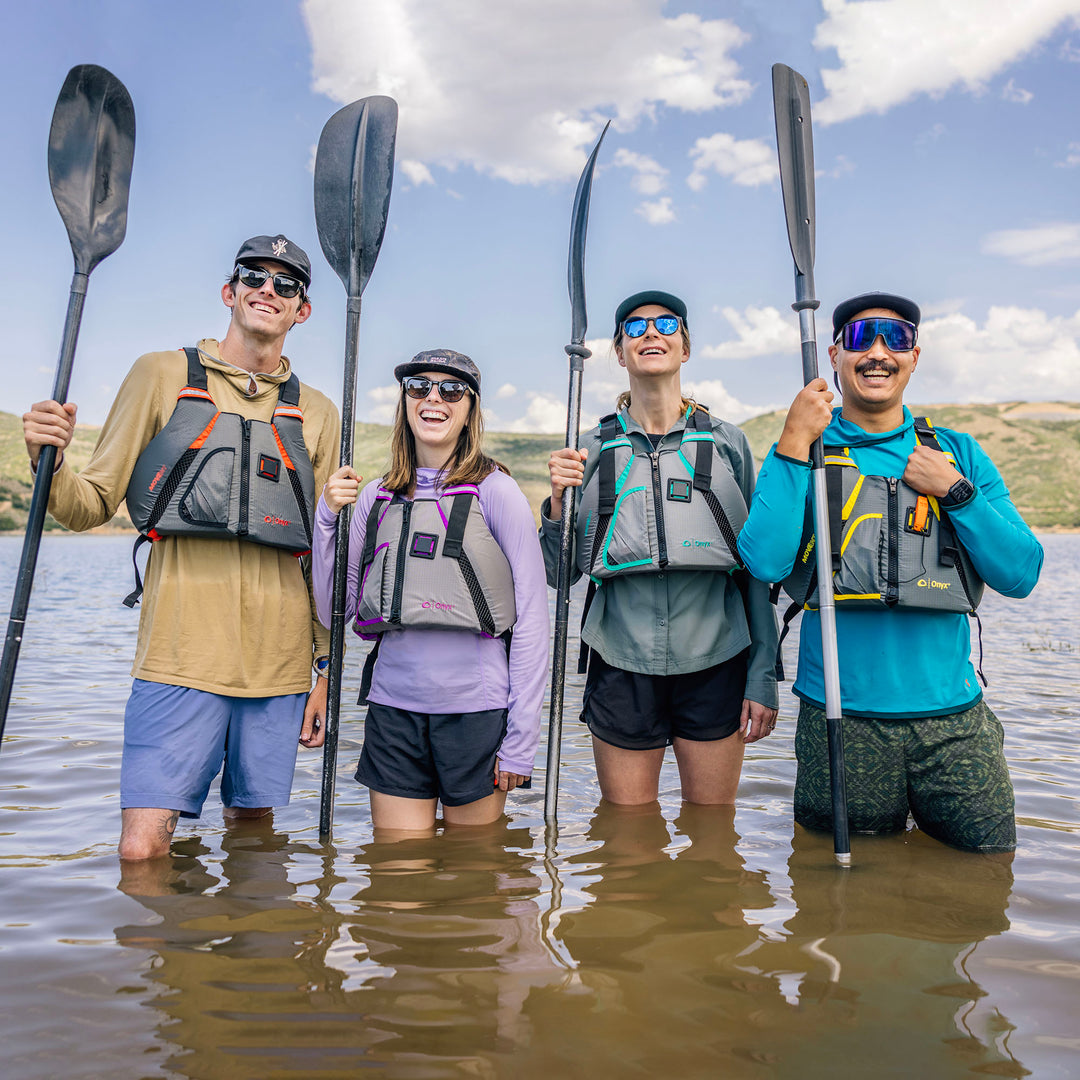 Four in MoveVent Dynamic Life Jackets holding paddles on a sunny lake.